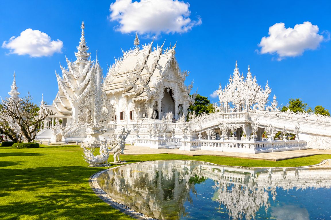 Beautiful Wat Rong Khun White Temple reflected in water under blue skies during a Chiang Rai Tours tour with our agency